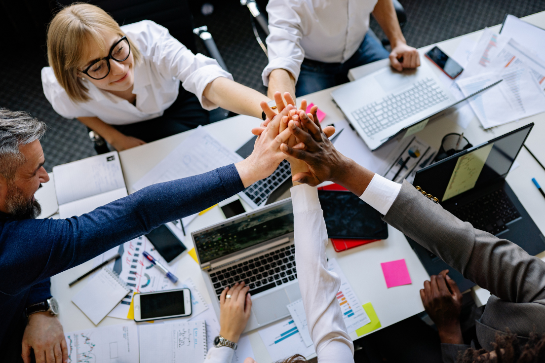Team celebrating collaboration with a group high-five at the office table.